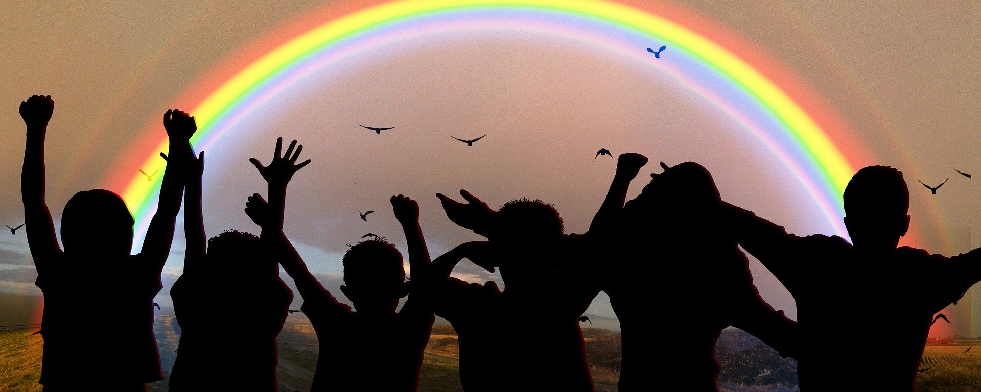 Silhouettes of children beneath a rainbow.